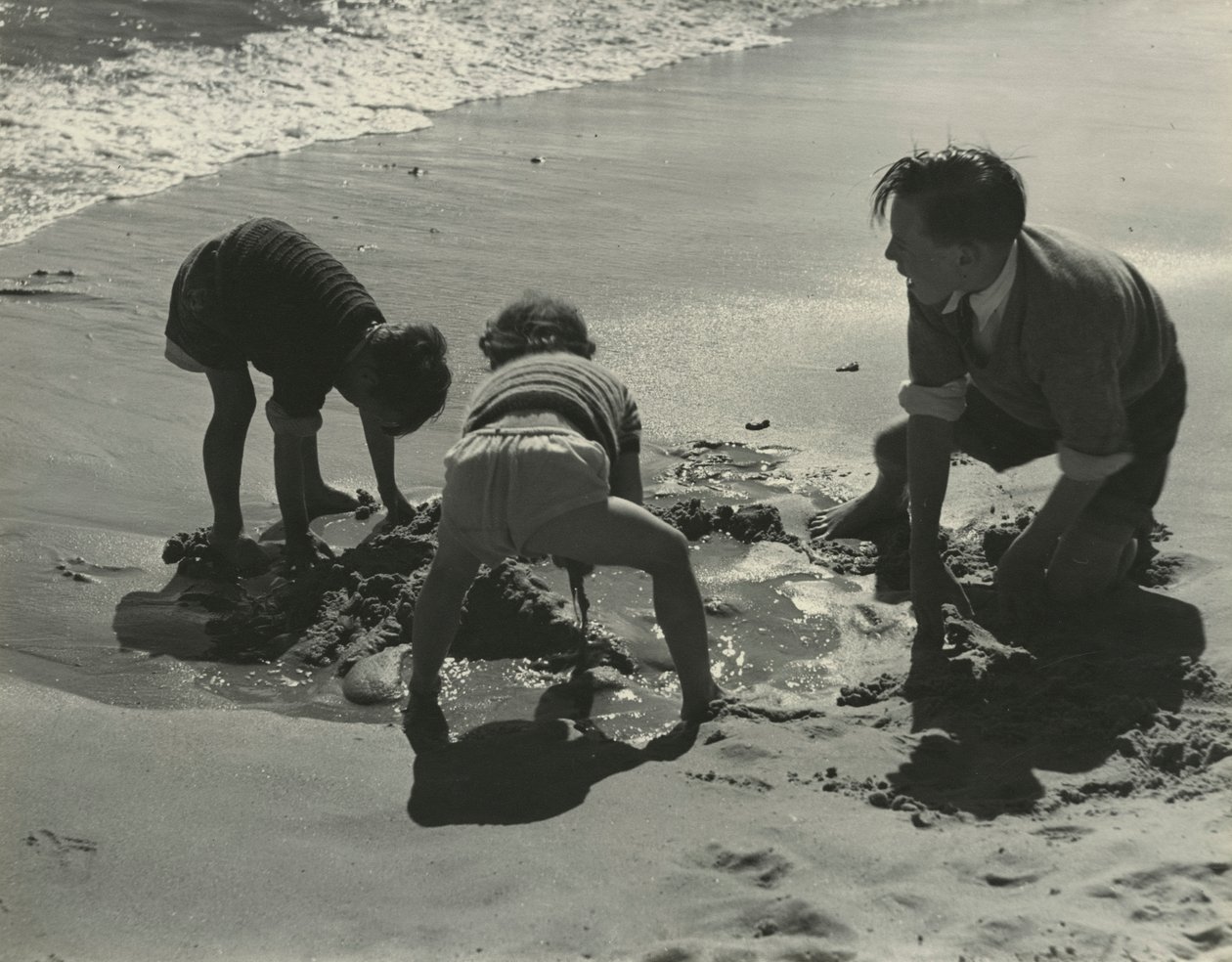 Tre barn leker med sand på stranden. av Godfrey Macdominic