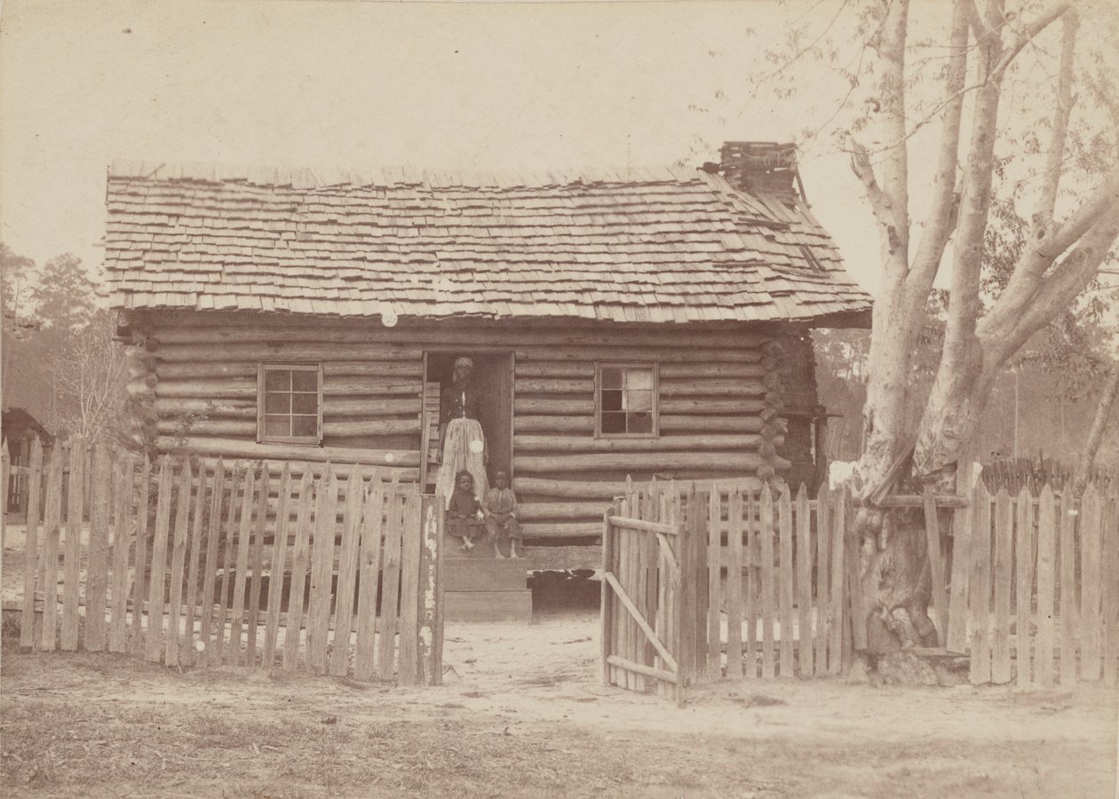 Albumintryck av en kvinna och två barn framför ett timmerhus i Georgia, 1880-talet. av H. S. Clark
