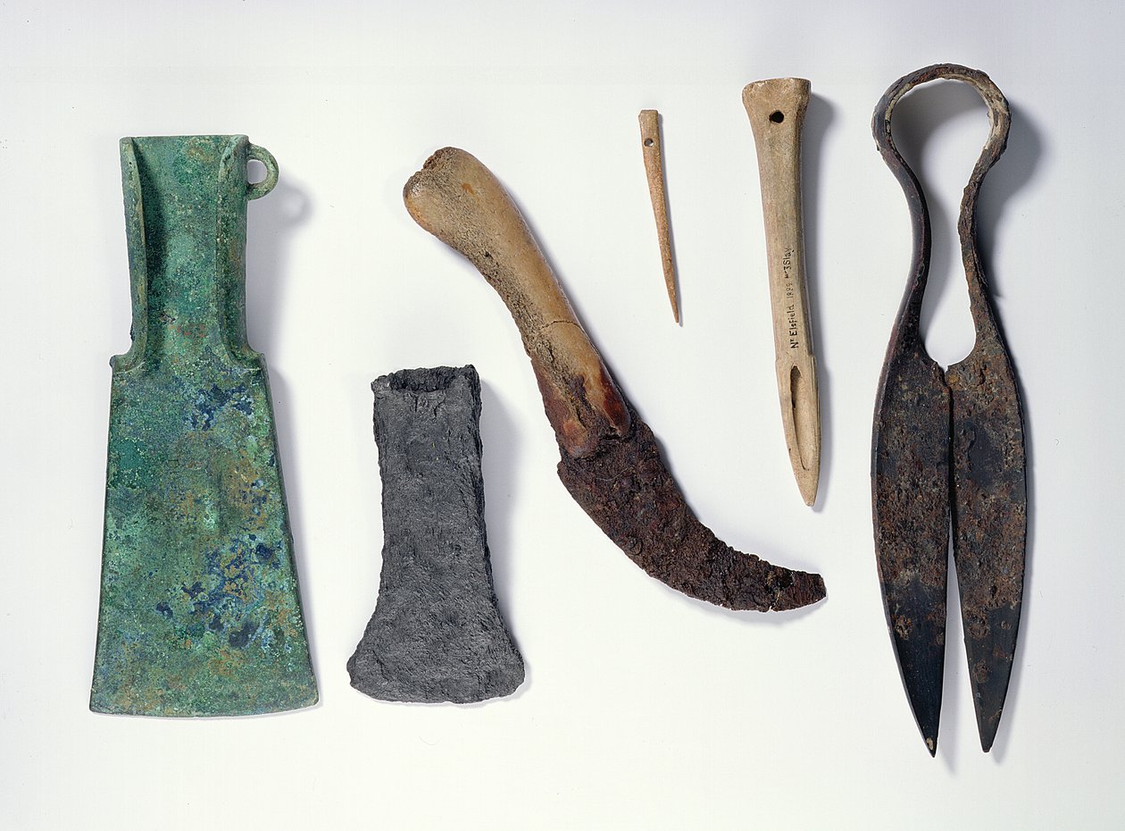 Urval av verktyg: L-R: bronsyxa från tidig järnålder med böjda vingar; senare järnyxa; kniv med benhandtag; bennål; bensyl; järnskivor av Iron Age