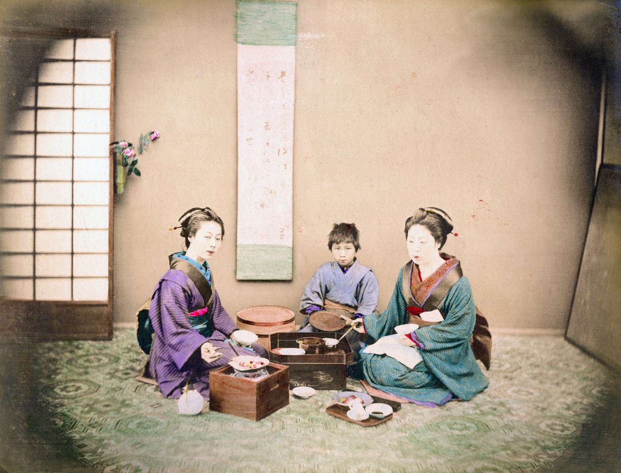 Två kvinnor och ett barn äter lunch, sittande på en matta, ca 1890 (handfärgat foto) av Japanese Photographer