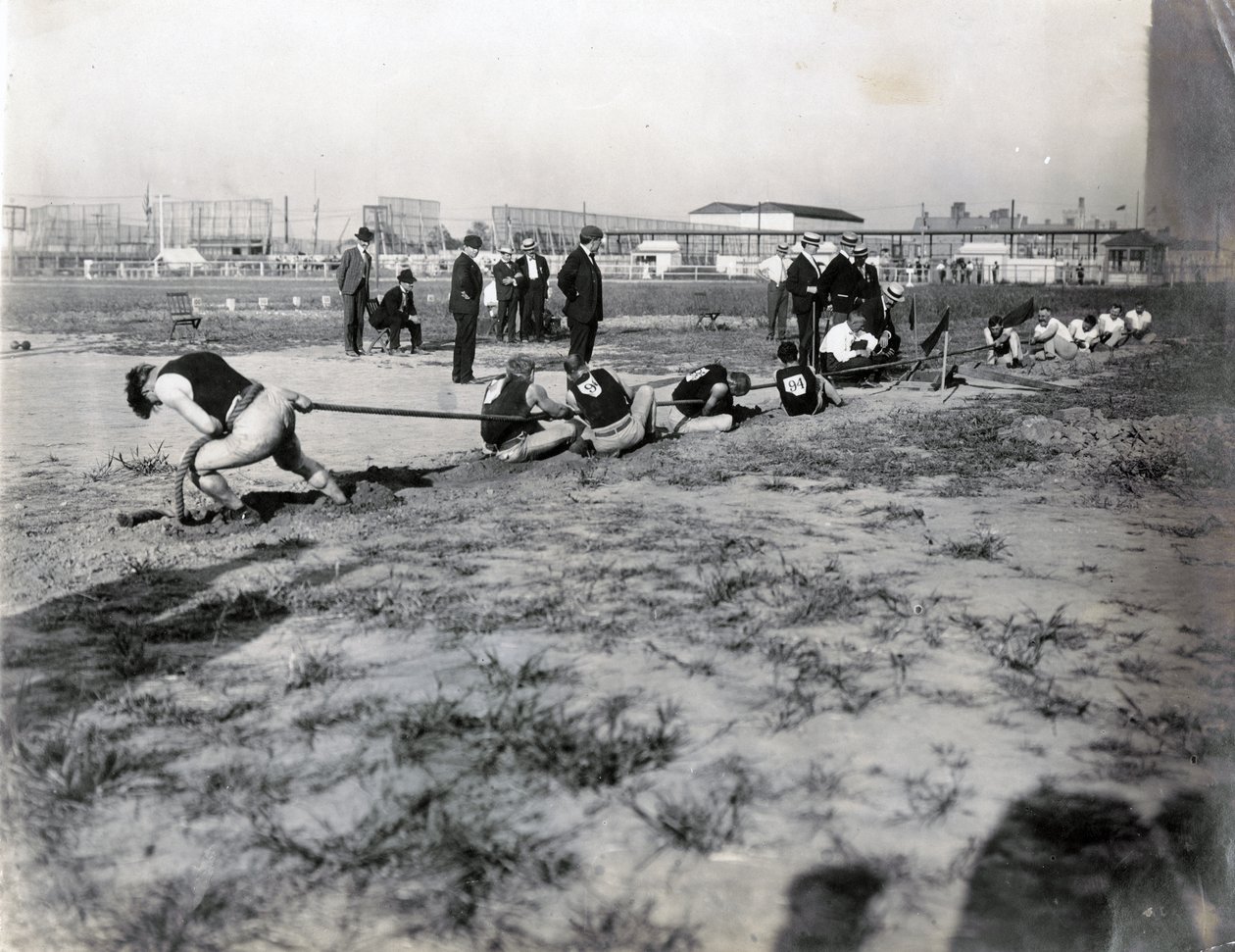 Horizontal photograph of two teams competing in tug of war. There are judges standing behind the rope. The shadows of spectators can be seen in the photograph av Jessie Tarbox Beals