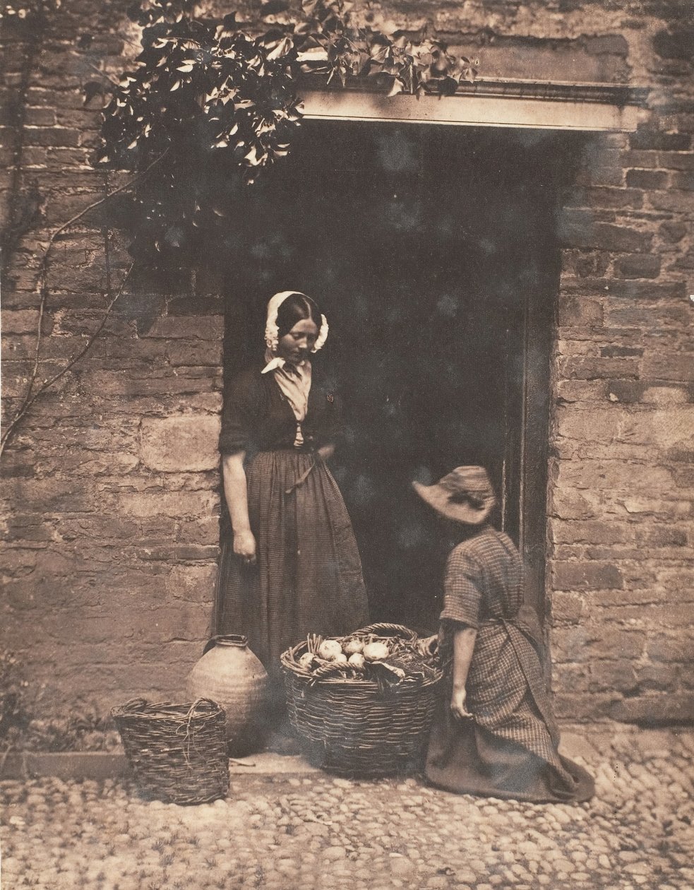 [Två kvinnor, en knästående och en stående, tittar i en korg fylld med grönsaker], 1853-56. av John Dillwyn Llewelyn