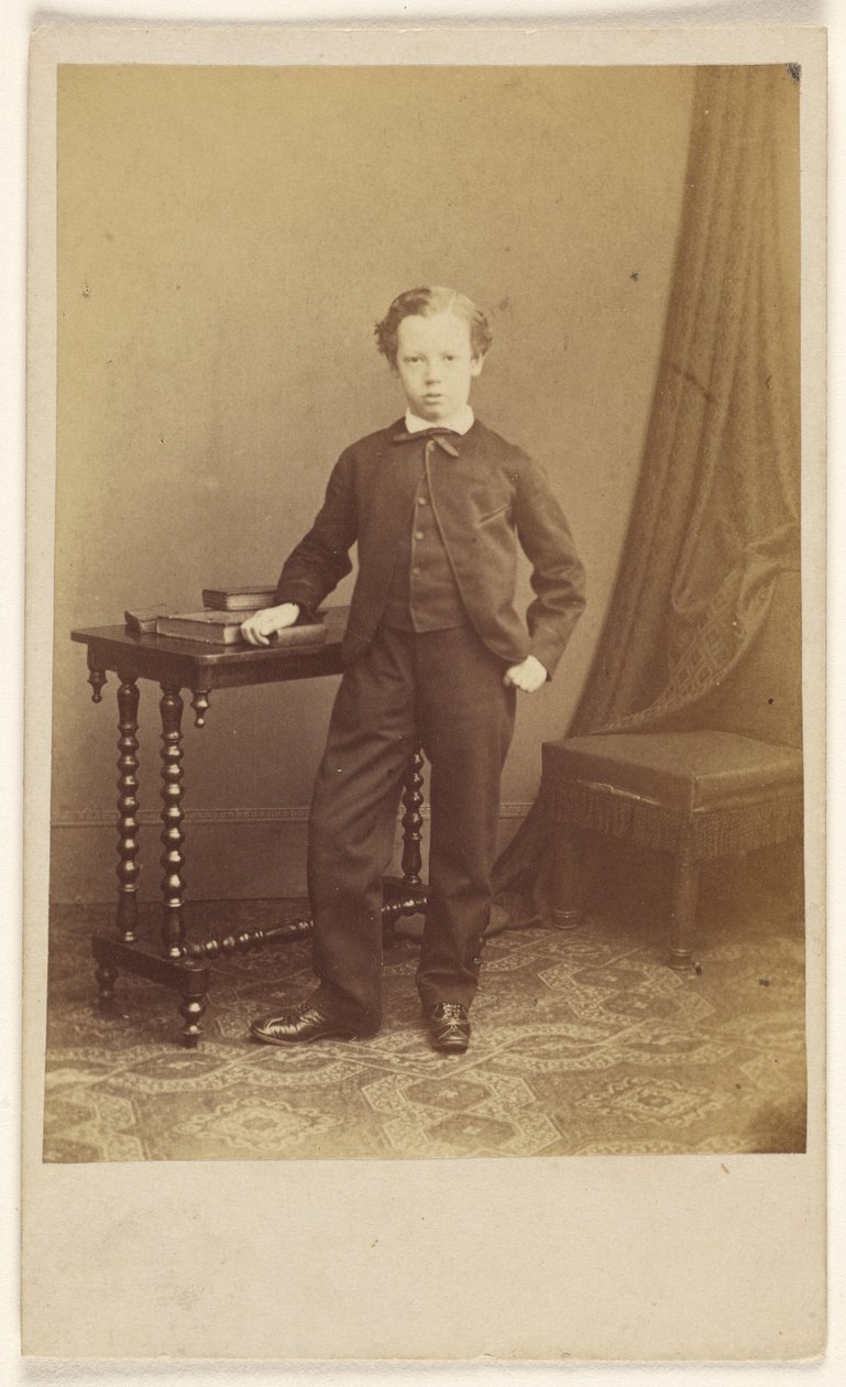 [Oidentifierad liten pojke i kostym står vid ett bord med böcker ovanpå] av Joseph Brown