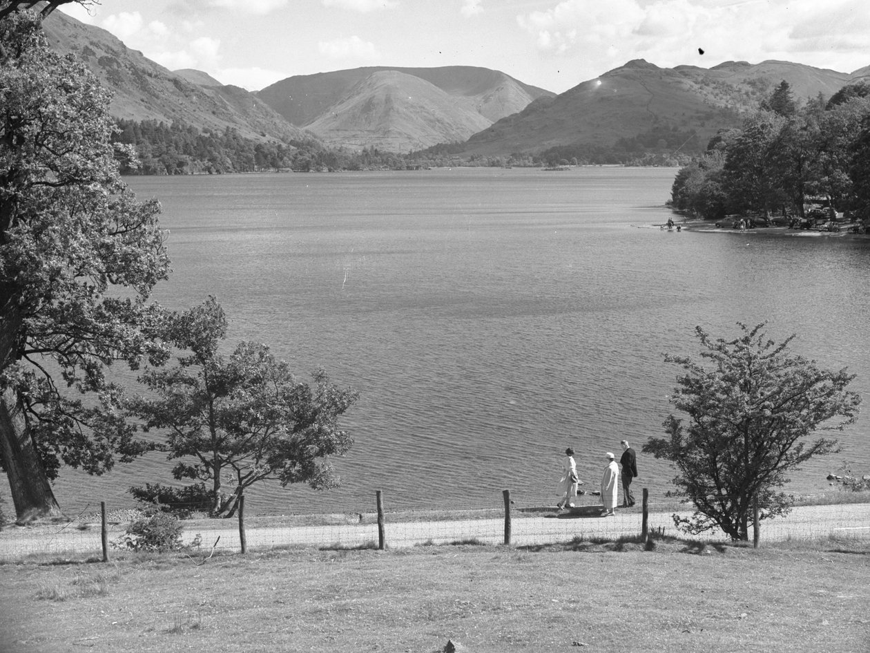 En man, en kvinna och möjligen deras dotter promenerar längs kanten av en sjö, med fjällen i bakgrunden av Joseph Hardman