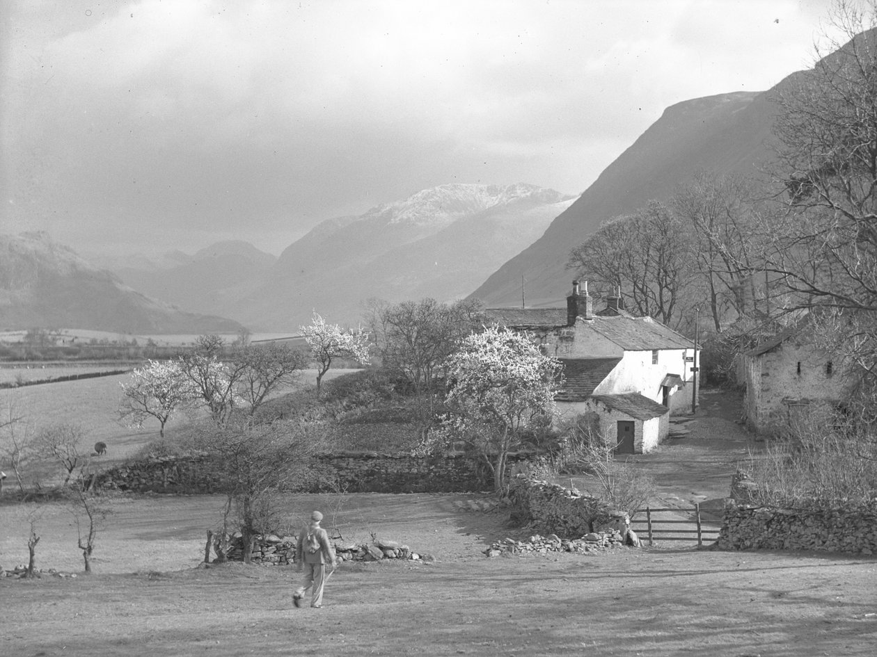 En man går mot en väg och Gillerthwaite House, med sjö och fjäll i bakgrunden av Joseph Hardman