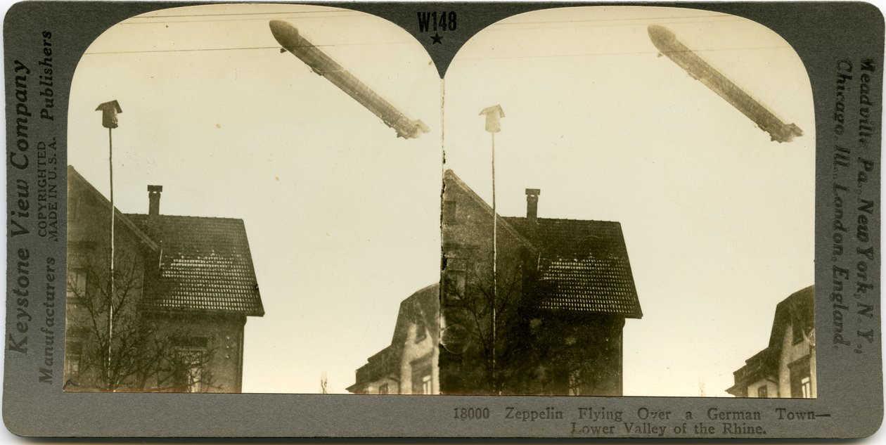 Horizontal, sepia stereocard showing a Zeppelin flying over the roofs of a town. Keystone Stereograph number 18000. The title reads av Keystone View Company