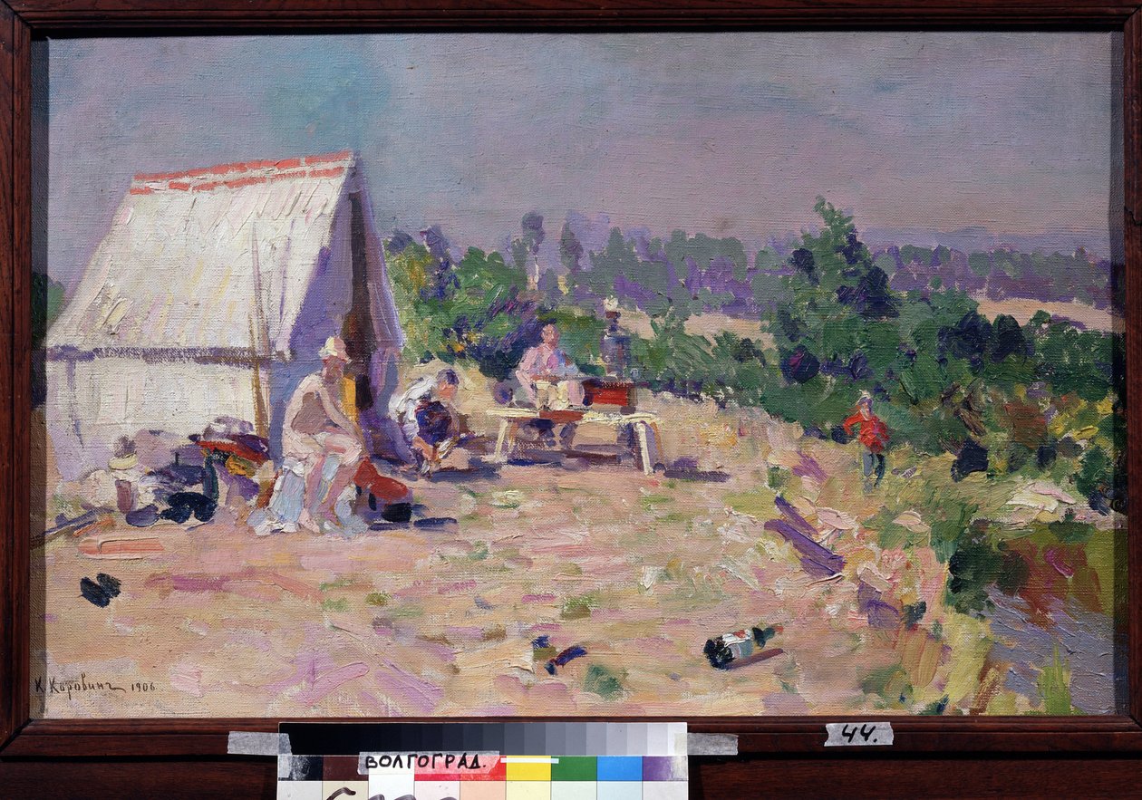 En picknick (picknick). (På picknick). Scen för familjelivet, vid kanten av en flod, ett tält och några hopfällbara möbler installeras i solen, för en utomhuslunch och en dag av avkoppling. En del skräp strödde ut marken. Målning av av Konstantin Alekseevich Korovin