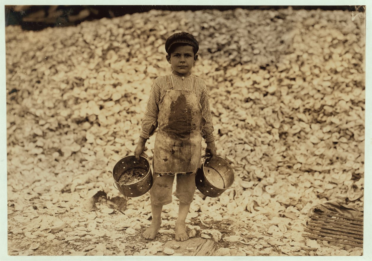Manuel, 5 år gammal, migrerande räkplockare framför en hög med ostronskal, arbetar för andra året på Dunbar, Lopez, Dukate Company, Biloxi, Mississippi, 1911. av Lewis Wickes Hine