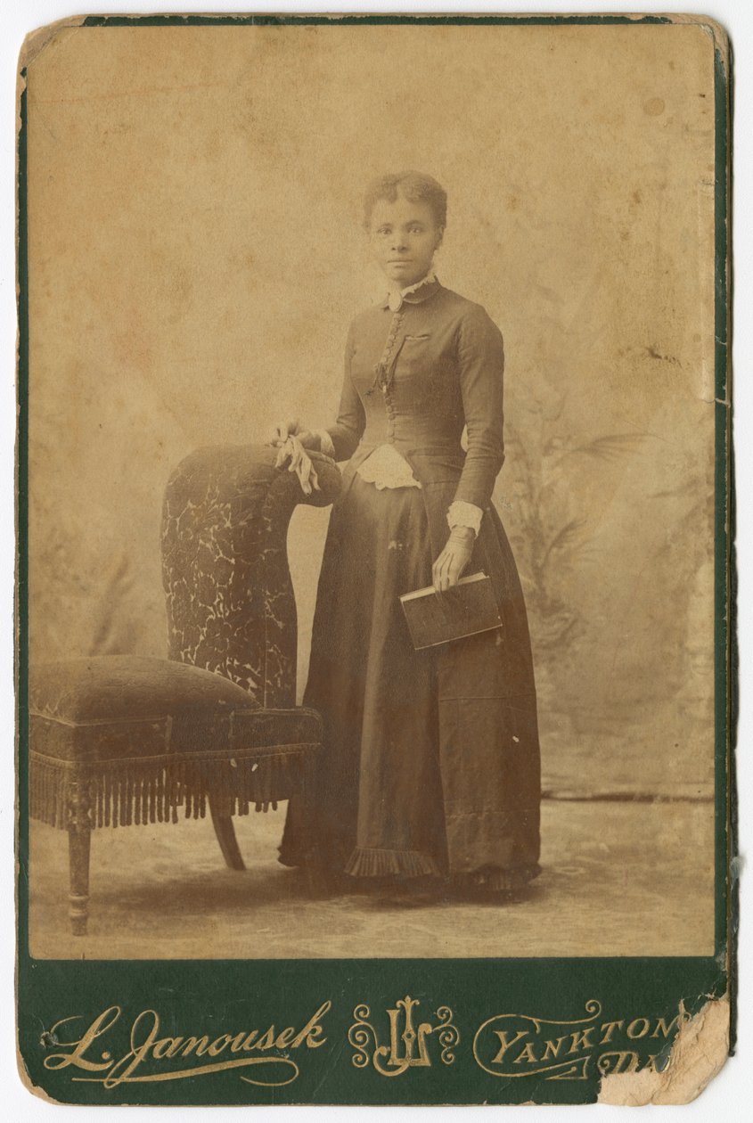 Fotografi av en kvinna som står bredvid en stol och håller i en bok, sent 1800-tal. av Louis Janousek