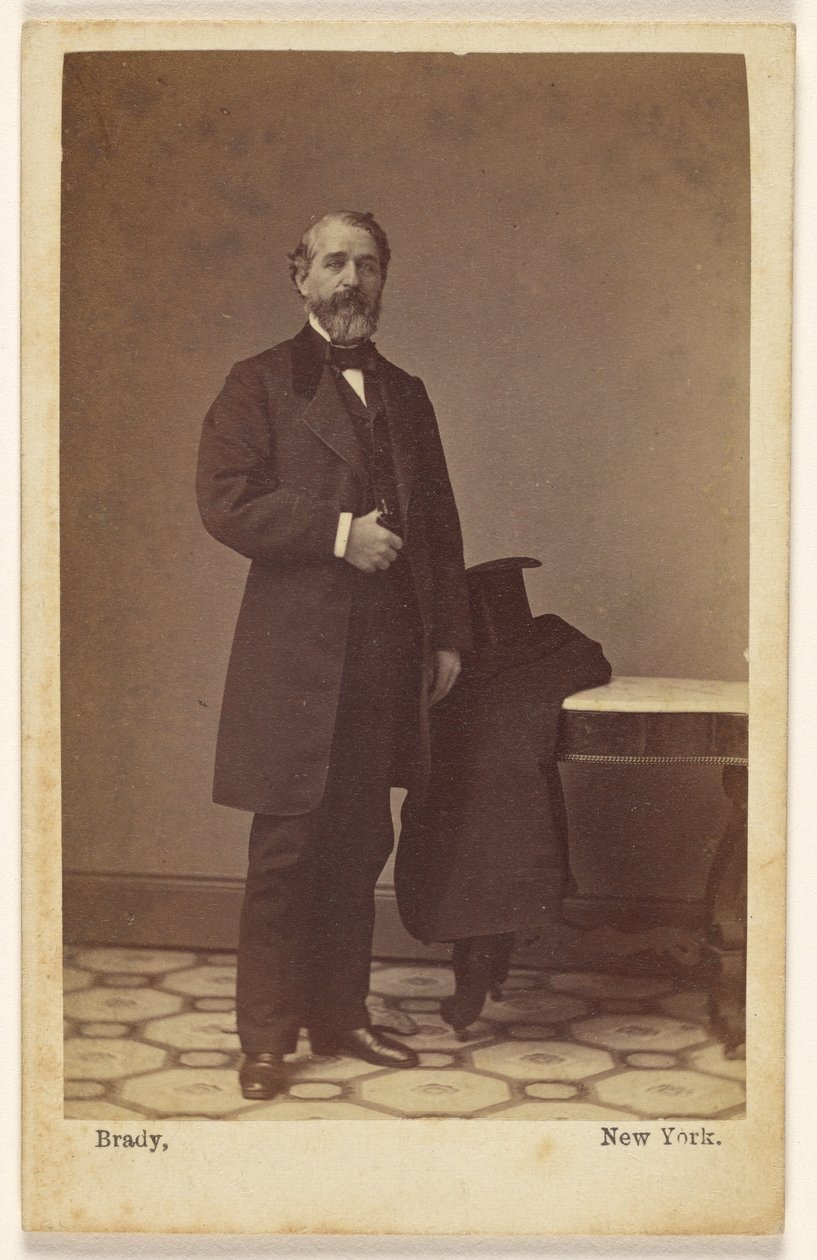 [En okänd skäggig man står upp; en hög hatt och en rock ligger på ett bord i närheten] av Mathew B. Brady