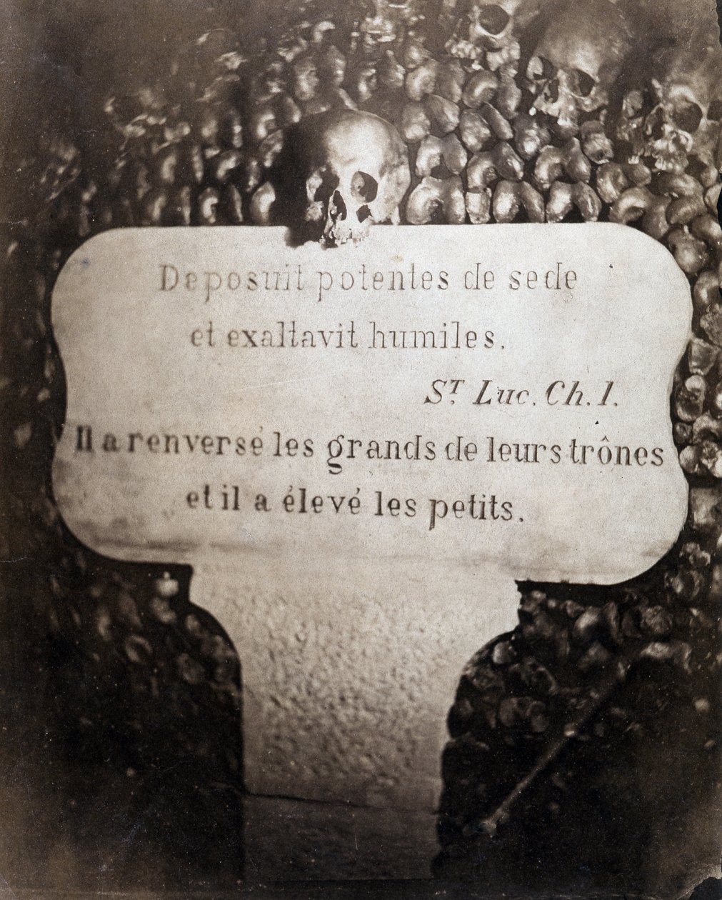 Ossuarierna i Paris katakomber. Petrus bär ett citat från kapitel 1 i Lukasevangeliet (Deposuit potentes de sede et exaltavit humiles. På franska: Han störtade de stora och uppfostrade de små) av Nadar