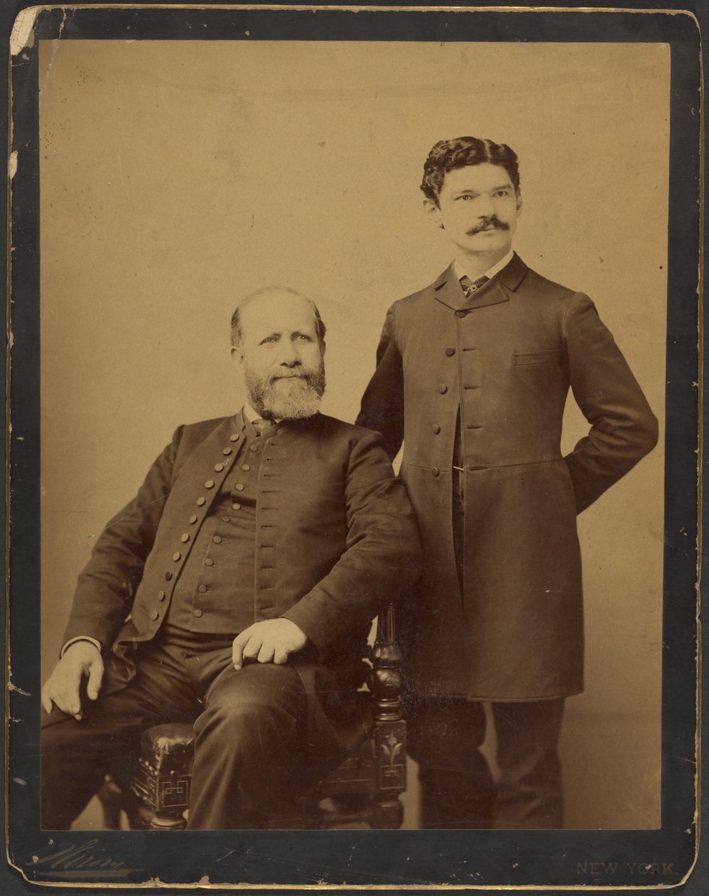 [En okänd skäggig man som sitter tillsammans med en okänd man med mustasch som står upp] av Napoleon Sarony