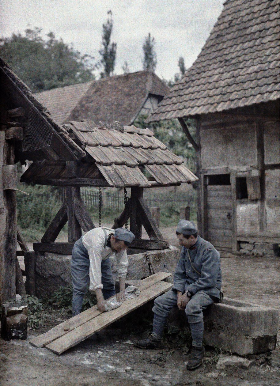 Två franska soldater tar hand om sin tvätt med hjälp av brädor som satts upp på tråget till en fontän nära en bondgård i staden Gildwiller, departement Haut-Rhin, Alsace, Frankrike, 21 juni 1917 (a av Paul Castelnau