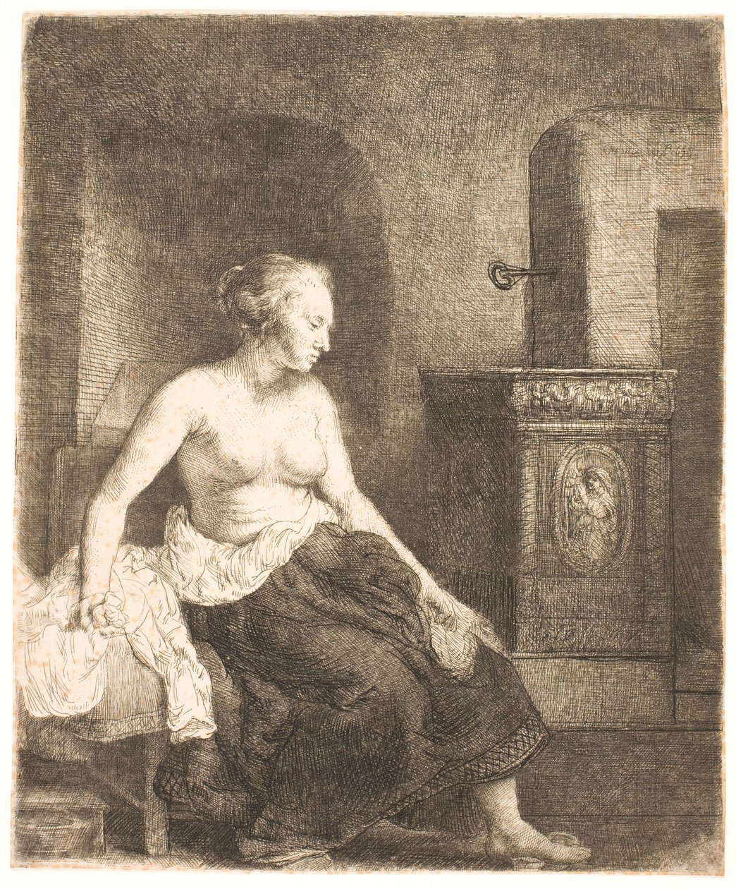 Kvinna som sitter halvklädd bredvid en spis av Rembrandt van Rijn