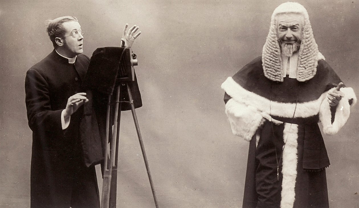 En man i en socka riktar linsen på sin kamera mot en man klädd som en påve av Rotary Photographic Co Ltd