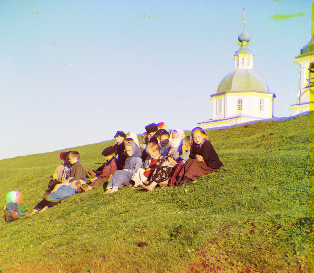 Ryska barn som sitter på sidan av en kulle nära en kyrka och ett klocktorn på landsbygden nära White Lake, i norra Europeiska Ryssland, 1905-1915 av Sergey Prokudin Gorsky