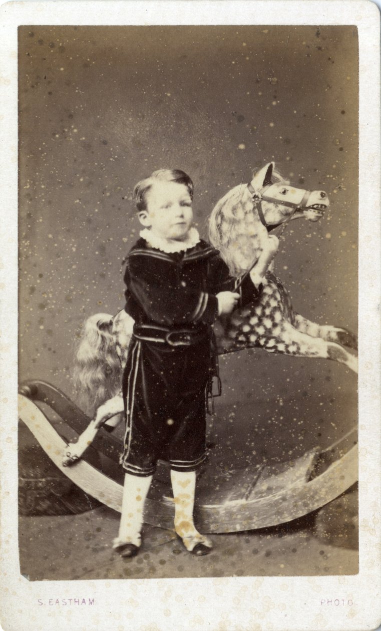 Ung pojke som står vid en gunghäst av Silas Eastham