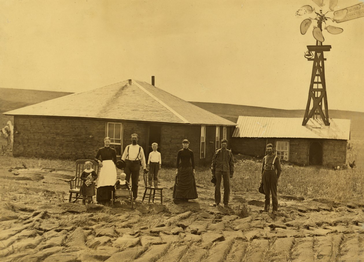 Hembygdsfamilj, utanför sitt torvhus med en väderkvarn på taket av den angränsande byggnaden i Custer County, Nebraska, ca 1885 (s/v foto) av Solomon D. Butcher