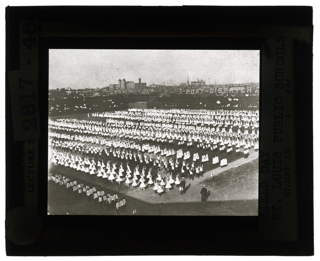 Horizontal, black and white photo of hundreds of school children lined up in formation for Field Day parade and pageant. All the girls in white dresses and the boys in white shirts and ties with dark pants av Unbekannt Unbekannt