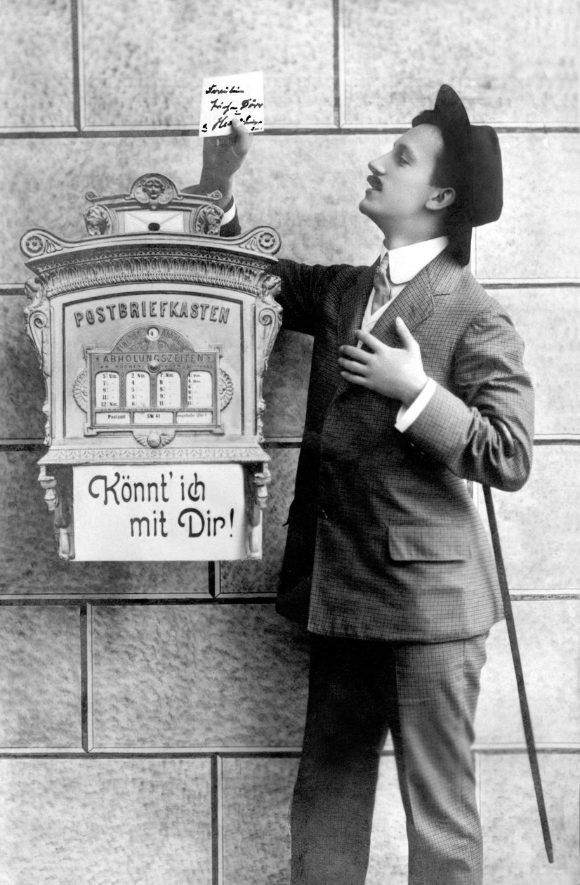 En elegant man i kostym, hatt och käpp, lägger upp en lapp i en brevlåda. Tyskland omkring 1920 Historiskt fotografi, man bredvid en brevlåda, omkring 1920 av Unbekannt