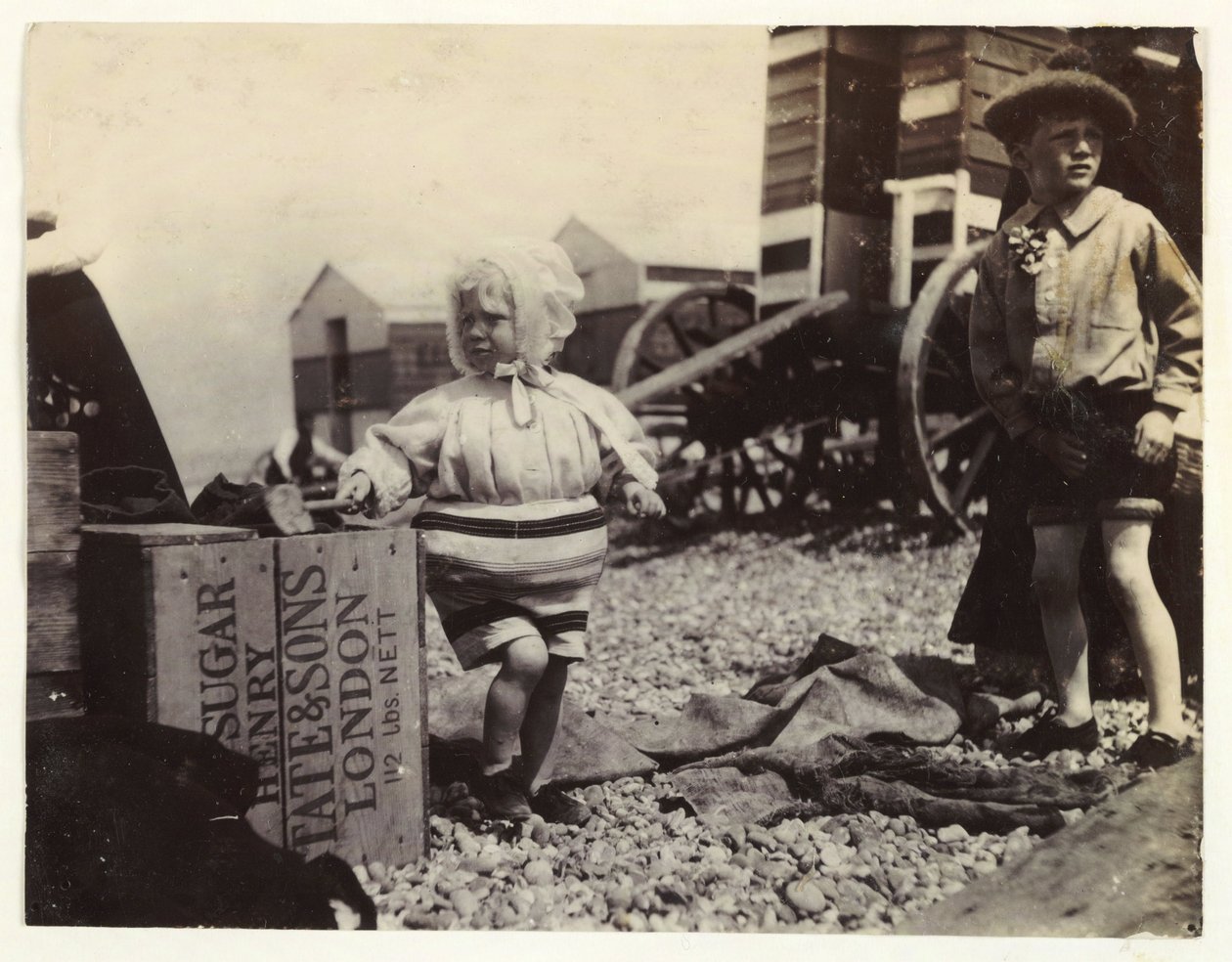 Två barn vid badmaskiner, c 1895, En ögonblicksbild av två barn vid havet, stående bland en grupp badmaskiner på stranden av Unbekannt