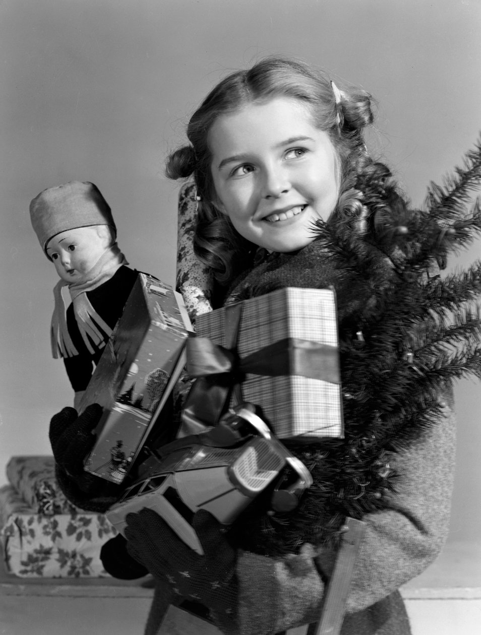 Ung flicka bär en armfull julklappar, c 1950 av Unbekannt