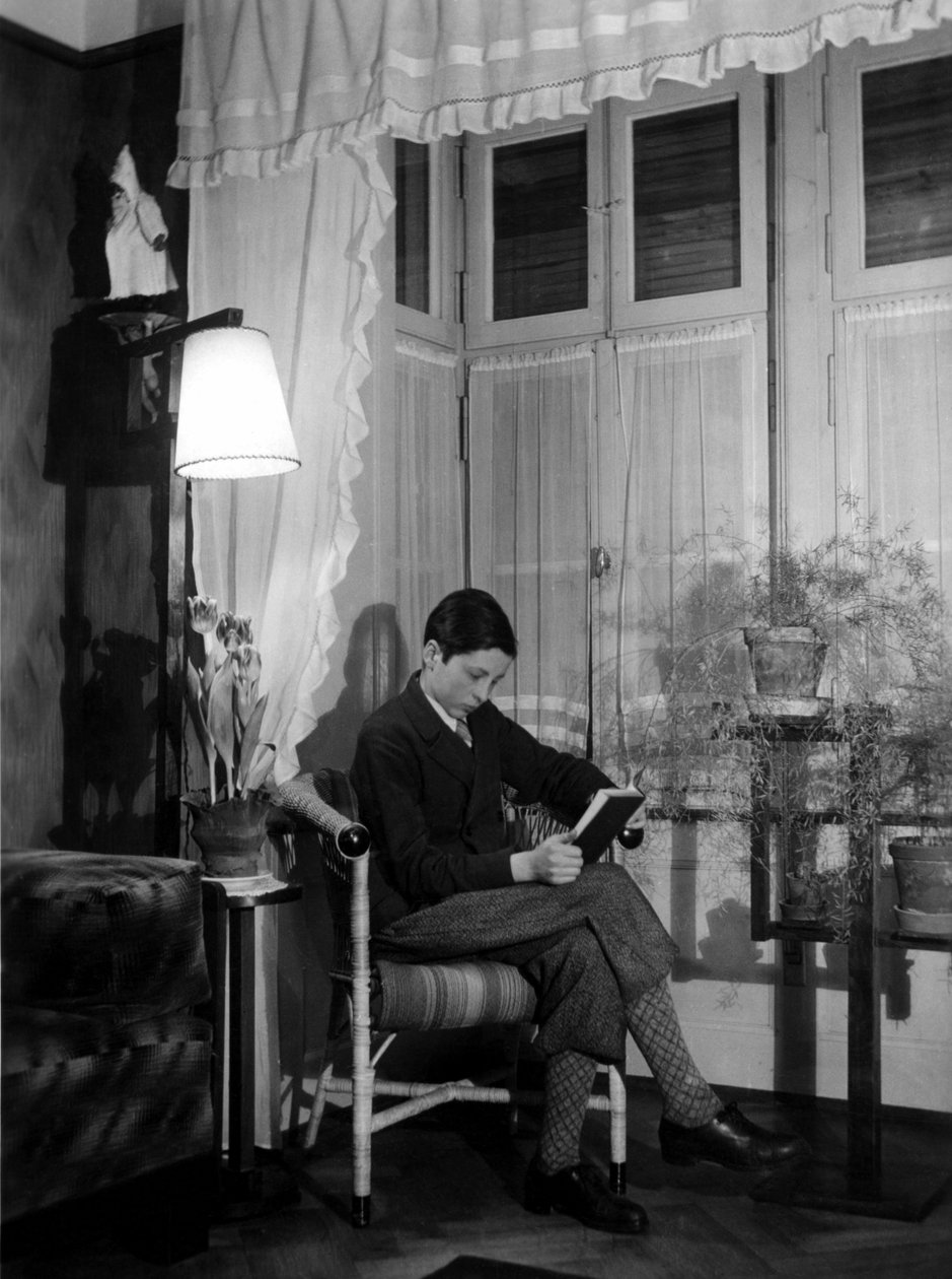 En tonåring sitter i en borgerlig interiör och läser en bok, bär kortbyxor och höga strumpor. 1915. Historiskt foto, kvinna som läser, ca 1915 av Unbekannter Künstler