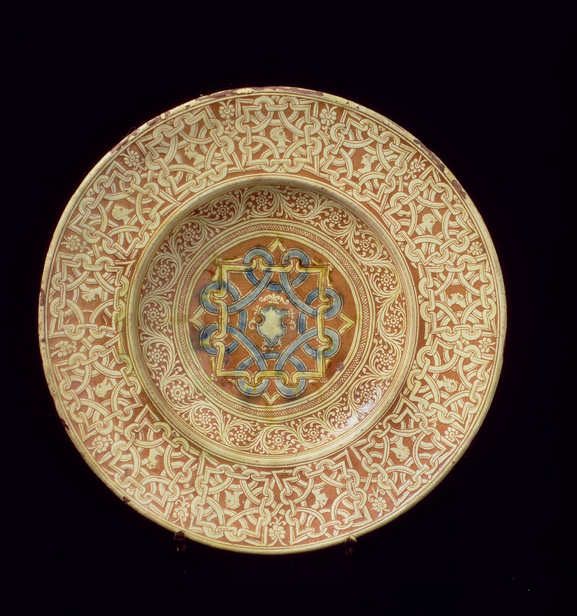 Maiolica-tallrik dekorerad med en utarbetad repetitiv knutdesign som ramar in profilhuvuden på gränsen och en sköld i den centrala plattan, italiensk, tillverkad i Toscana av Unknown
