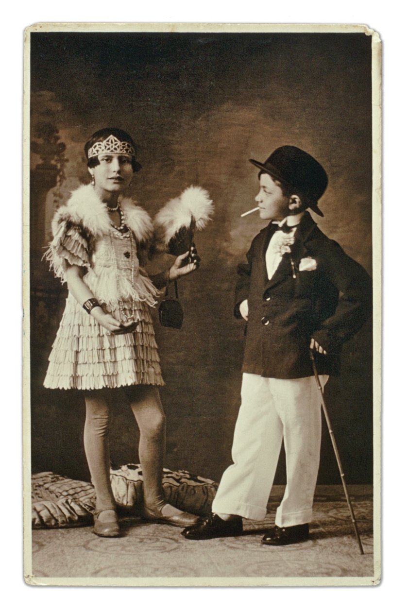 Två barn klädda som en vuxen klädd i 1920-talets mode, den lilla flickan bär en outfit för Charleston, och han i kostym, bowlerhatt och cigarett. Fotografi av Unbekannter Künstler