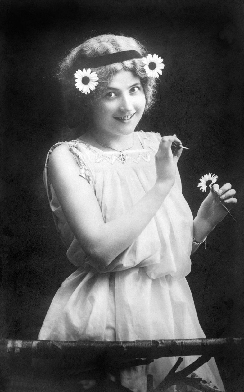 Kvinna som drar kronblad från en blomma: "" Han älskar mig. Han gillar inte mig. Han älskar mig...” Fotografering omkring 1912 av Unbekannt