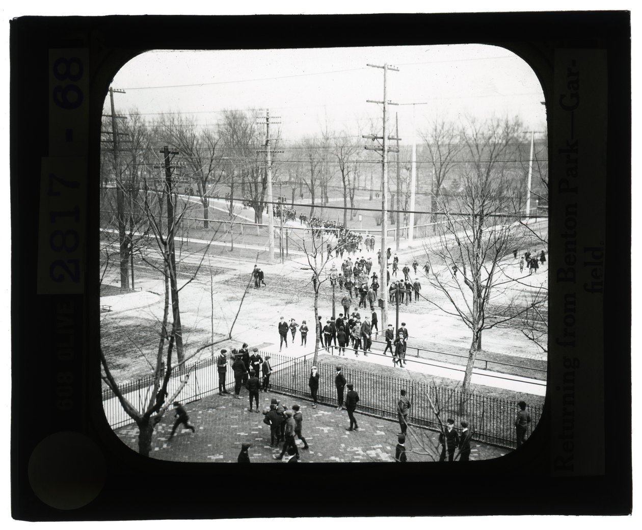 Horizontal, black and white photo of boys and girls crossing the street to return to school from a trip to the park av Unknown