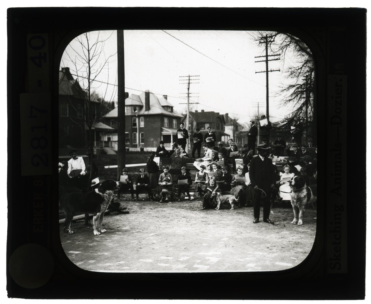 Horizontal, black and white photo of students drawing dogs in an outdoor classroom setting av Unknown