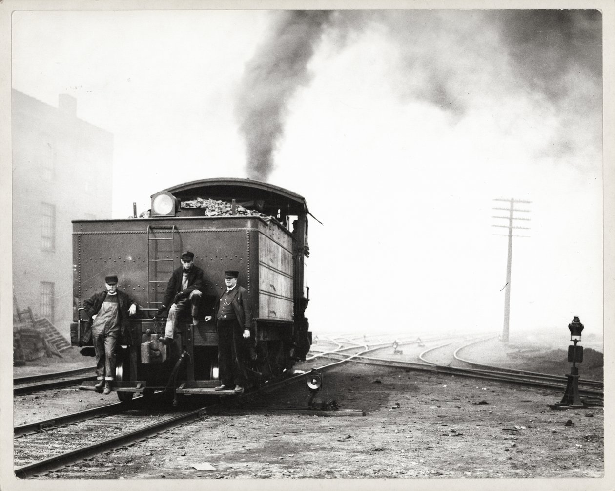Three men on the back of a switch engine in an unidentified rail yard av Unknown