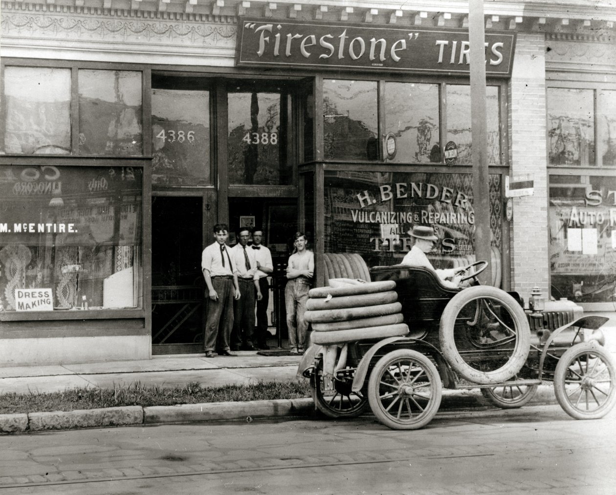 Men and automobile tire repair truck gathered outside the H. Bender Firestone Tire dealership at 4388 Olive Street av Unknown
