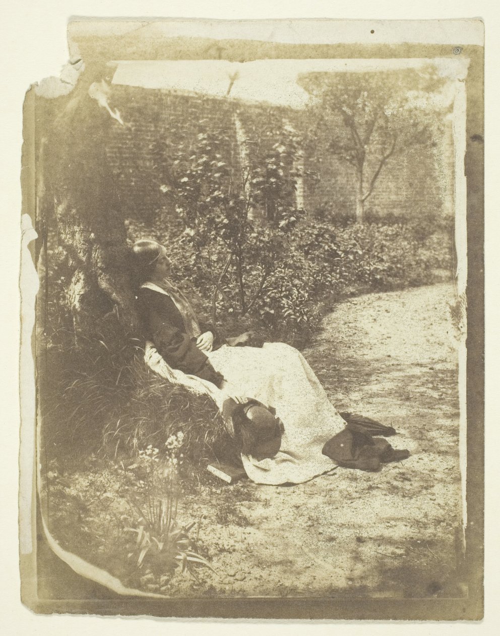 Mrs Craik liggande i trädgården med hatt och bok av Unknown