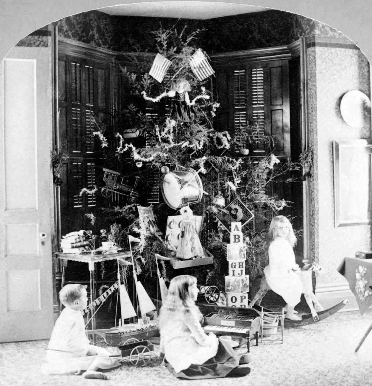 Barn samlades vid foten av trädet omgivna av presenter på julmorgonen. av Unknown photographer