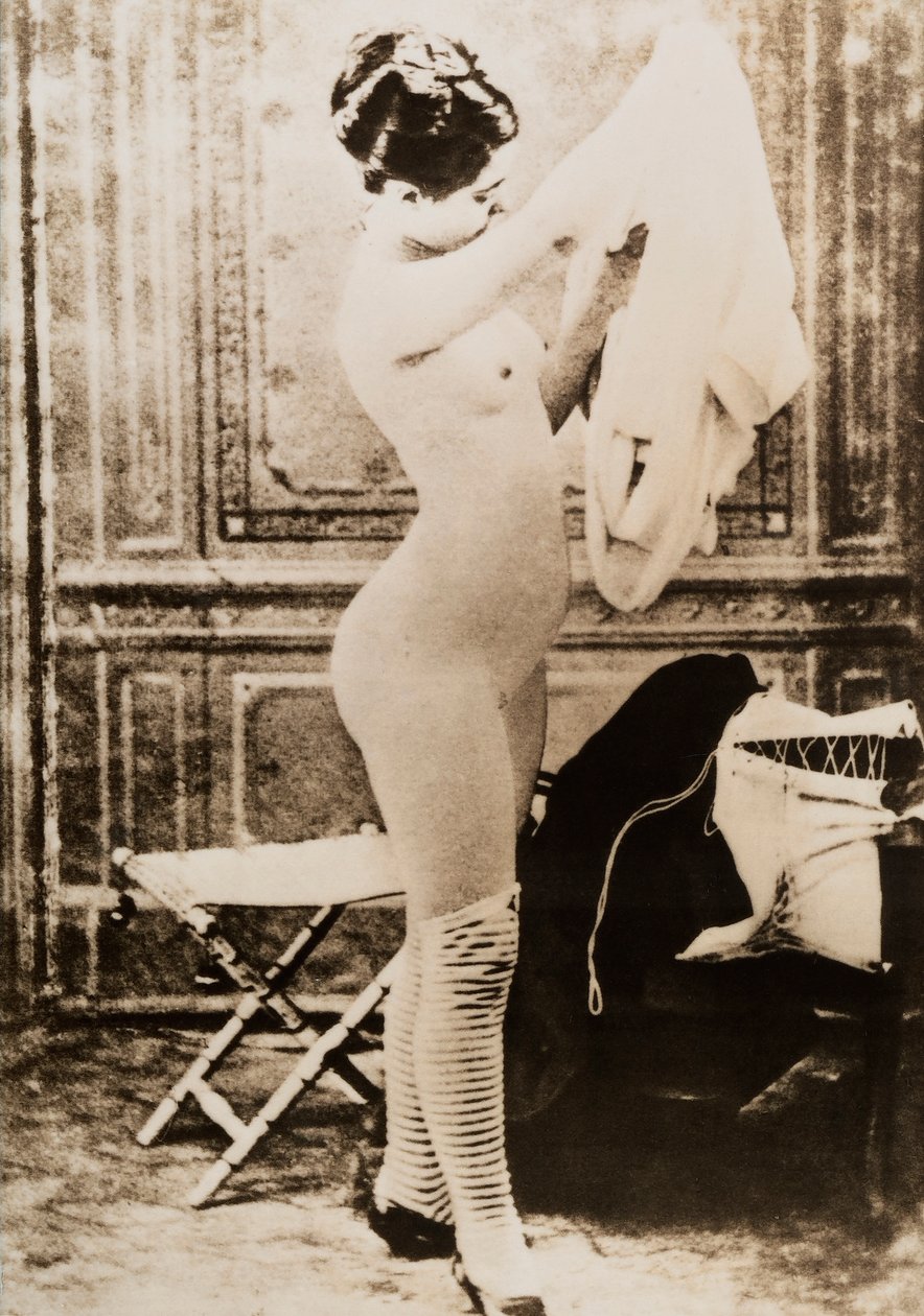 Nakenporträtt i helfigur av en ung kvinna som klär på sig. av Unknown photographer