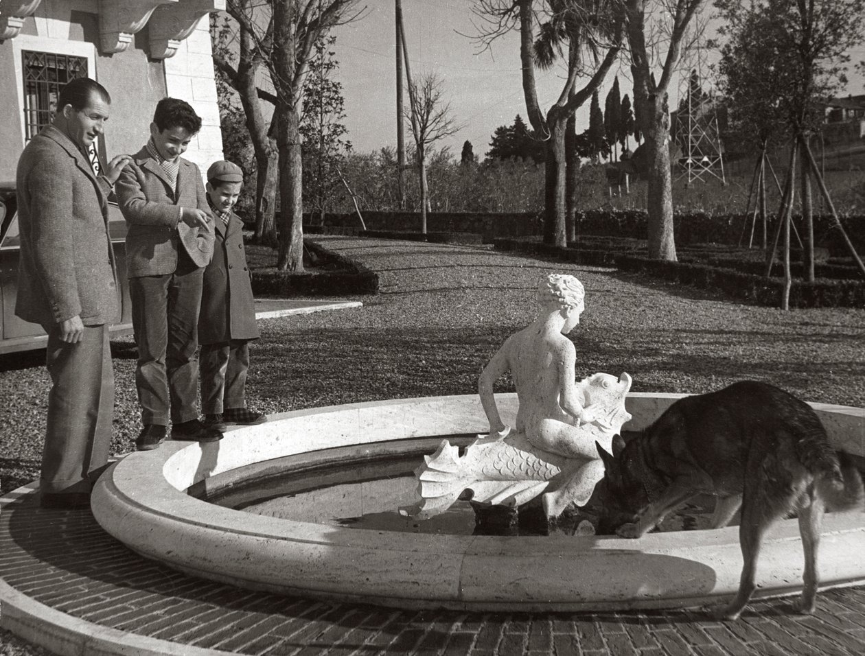 Gino Bartali med två barn och en hund nära en fontän av Unknown photographer