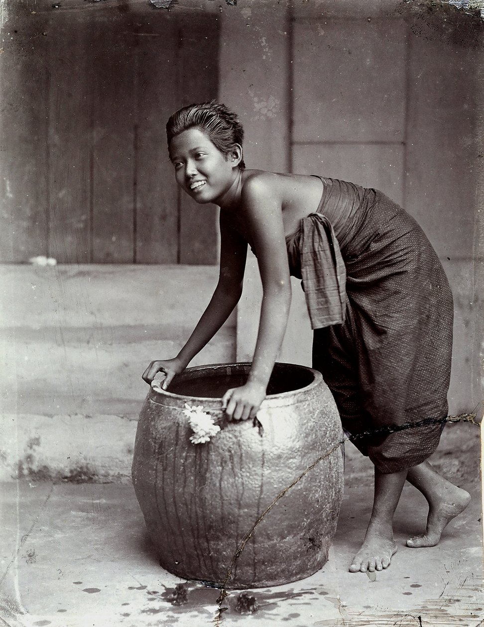 Ung leende thailändsk kvinna som lyfter en stor container av Unknown photographer