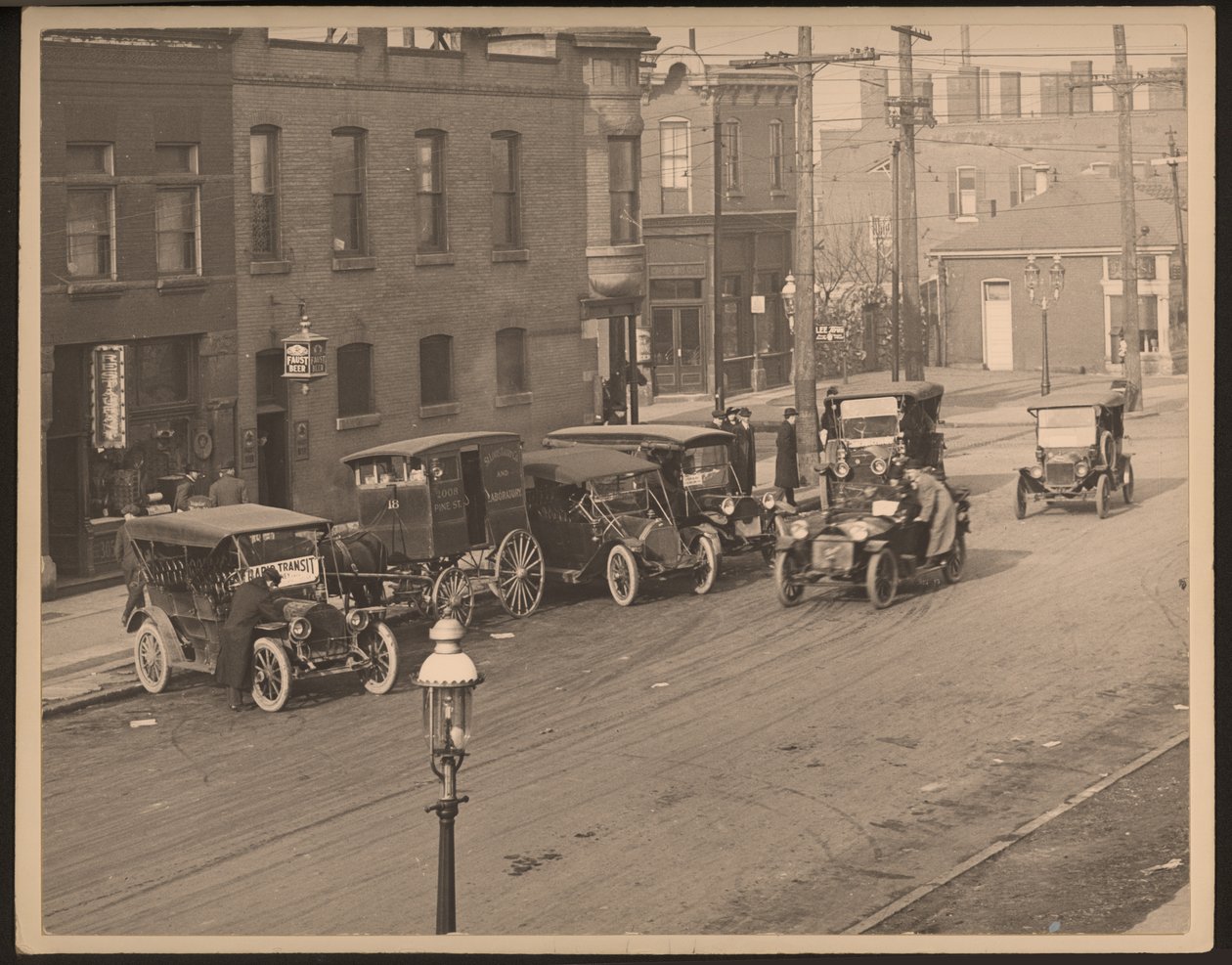 View of unidentified street with several automobiles and a horse-drawn delivery wagon from the St. Louis Bakery Company parked along the curb av William G. Swekosky