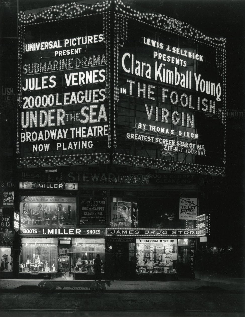 1554 Broadway på 46th Street, I. Miller Shoes; James Drug Store och stora tält för filmer lyser upp ovan. av William Davis Hassler