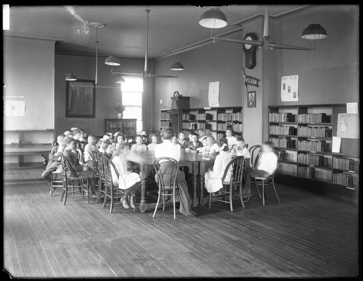 Barn lyssnar på en kvinna i läsrummet i en oidentifierad filial av Queens Borough Public Library, ca 1910 (s/v foto) av William Davis Hassler