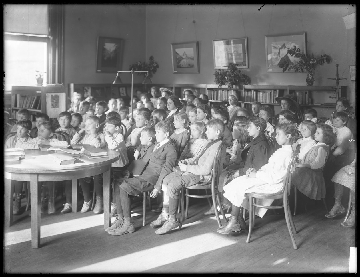 Barn som sitter och lyssnar i läsesalen i en oidentifierad filial av Queens Borough Public Library, ca 1910 av William Davis Hassler