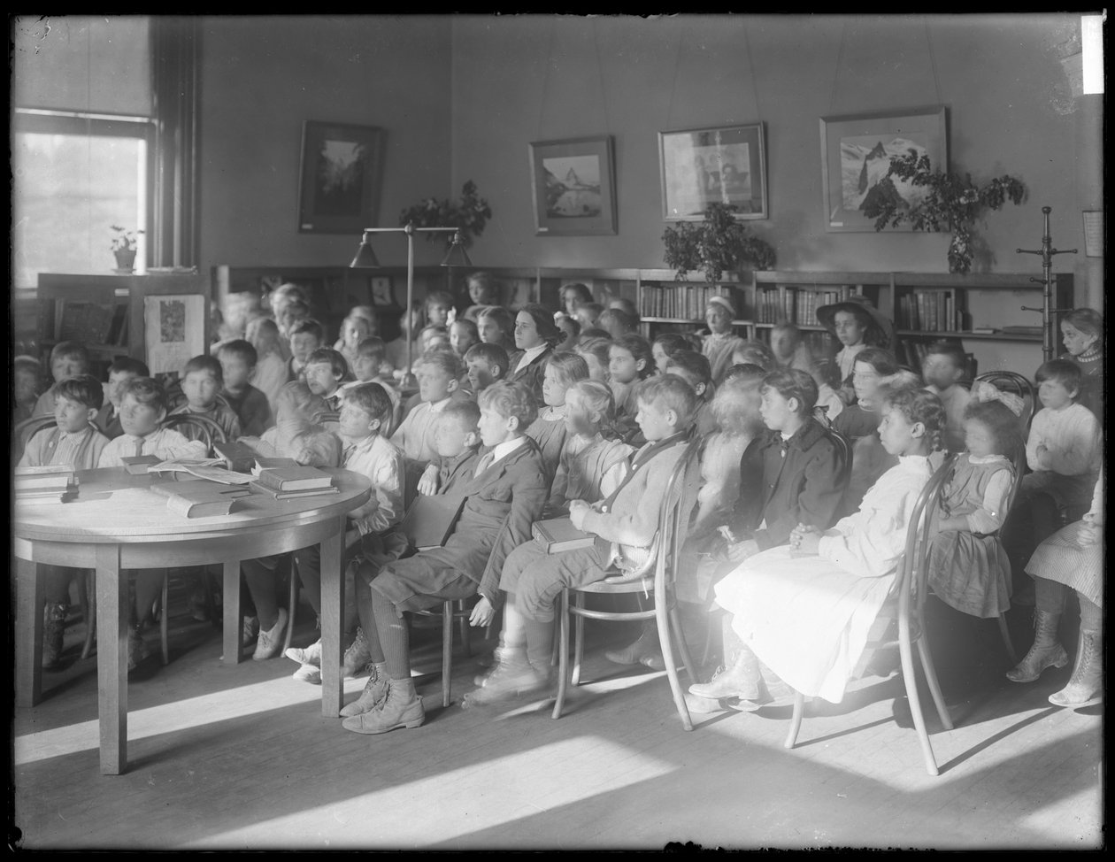 Barn som sitter och lyssnar i läsesalen i en oidentifierad filial av Queens Borough Public Library, ca 1910 av William Davis Hassler