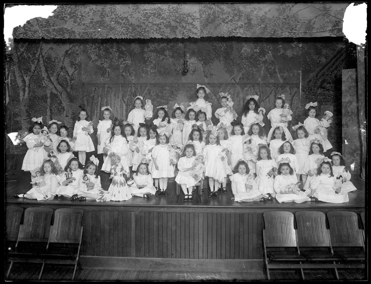 Grupp av små flickor som poserar på en liten scen med dockor i handen, troligen från det romersk-katolska barnhemmet, Kingsbridge, Bronx, omkring 1911. av William Davis Hassler