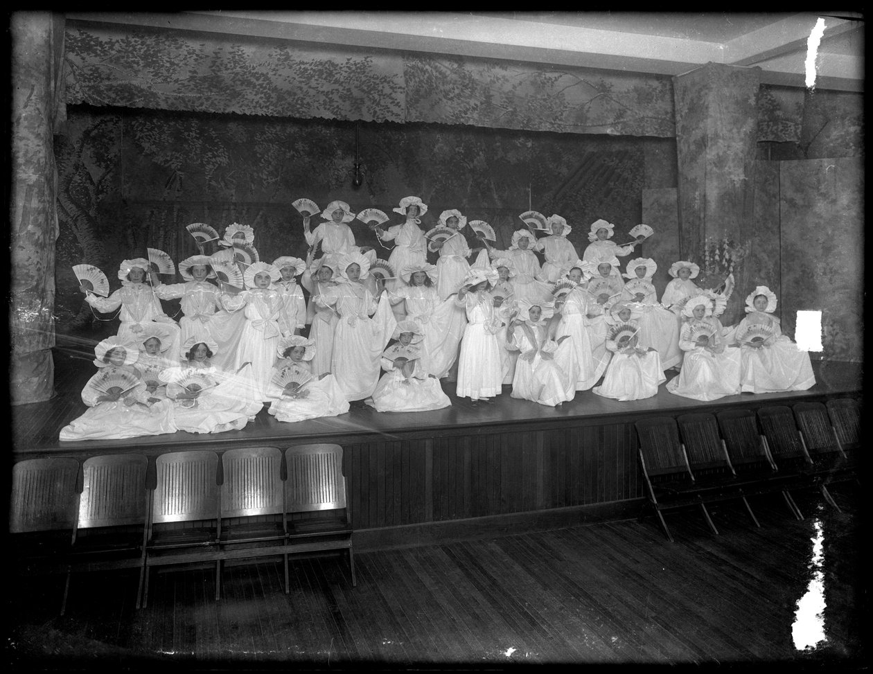 En grupp små flickor poserade på en liten scen med fans, förmodligen det romersk-katolska föräldrahemmet, Kingsbridge, Bronx, ca 1911 av William Davis Hassler