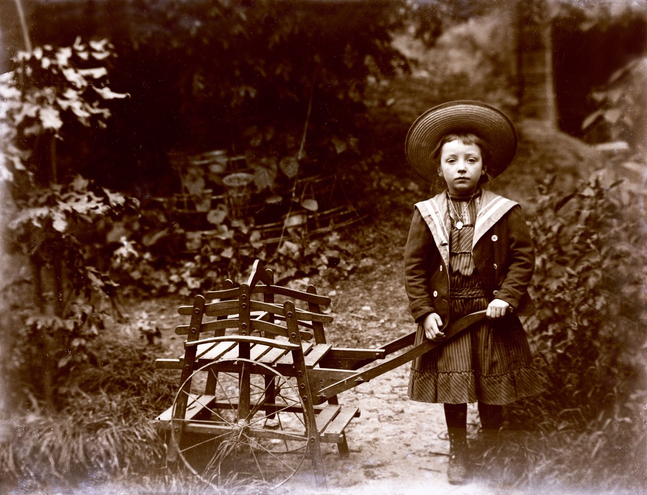 Flicka med vagn i en trädgård, tidigt 1900-tal (s/v foto) av . .