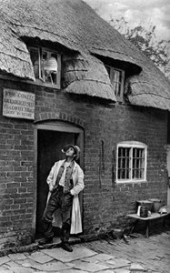 En man röker pipa utanför en butik, Worcestershire, c1922. av A. W. Cutler