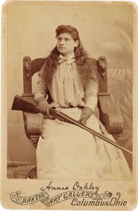 Annie Oakley: Annie Oakley:. Här sitter den legendariska skarpskytten ganska ödmjukt i en massiv stol i renässansstil, ett hagelgevär vilande i hennes knä. Hennes ömtåliga feminina drag och flytande hår motverkar hennes robusta utomhusbild ©Buyenlarge/UIG/ av American Photographer