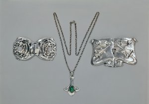 Silversmycken designade för Liberty. Vänster till höger: Midjelås med sammanflätad keltisk design, 1904. Hänge och kedja med cabochonskuren krysopras. Midjelås med repouse-design på hamrad